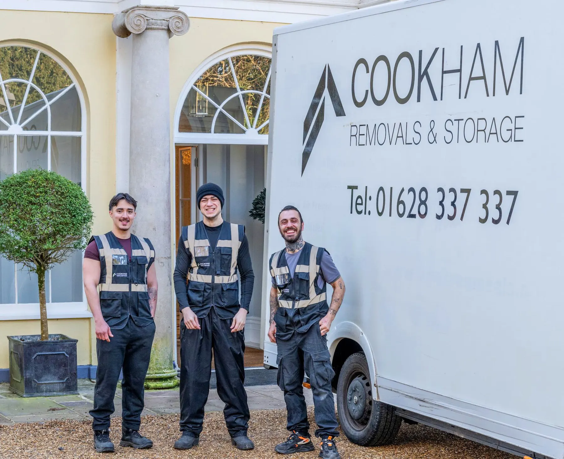 Three Cookham Removals & Storage crew members in branded grey vests standing by the white Luton van outside a house