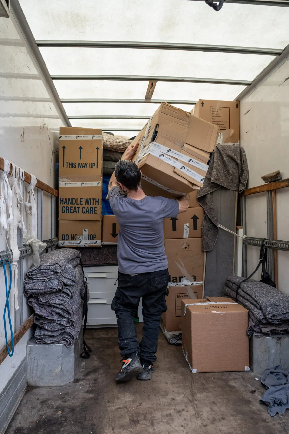 A Cookham Removals & Storage crew member inside the open Luton van lifting a box onto stacked boxes and removal blankets