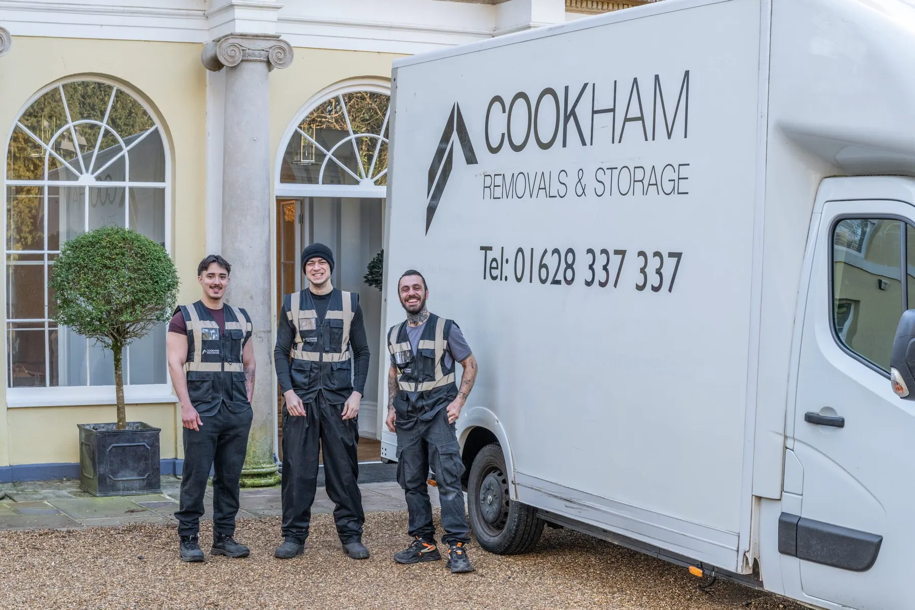 Three Cookham Removals & Storage crew members in branded grey vests standing in front of the Luton van at the Georgian house
