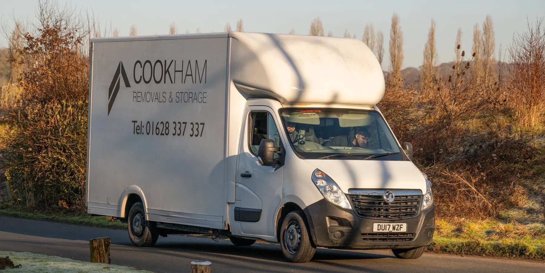 The white Cookham Removals & Storage Luton van driving along a road between hedges