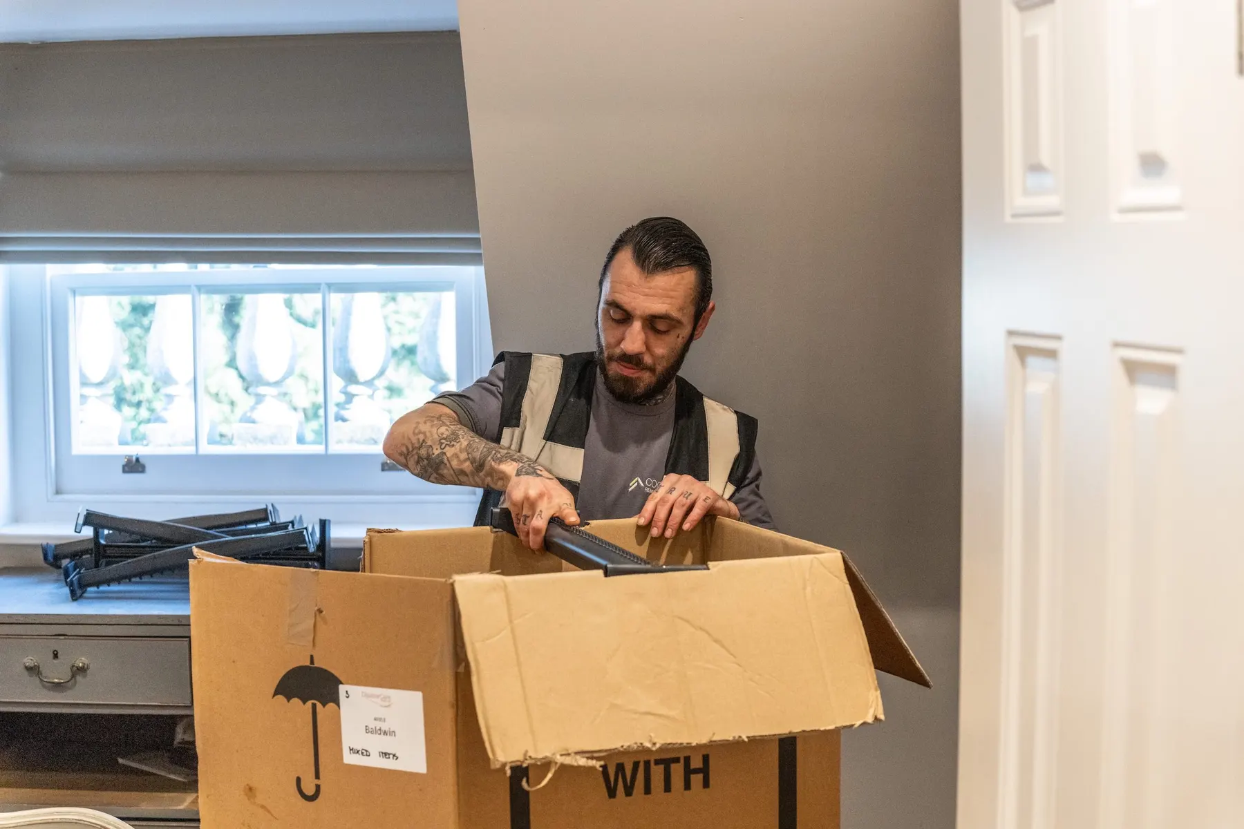A Cookham Removals & Storage crew member folding the flaps of a cardboard box in a bright room