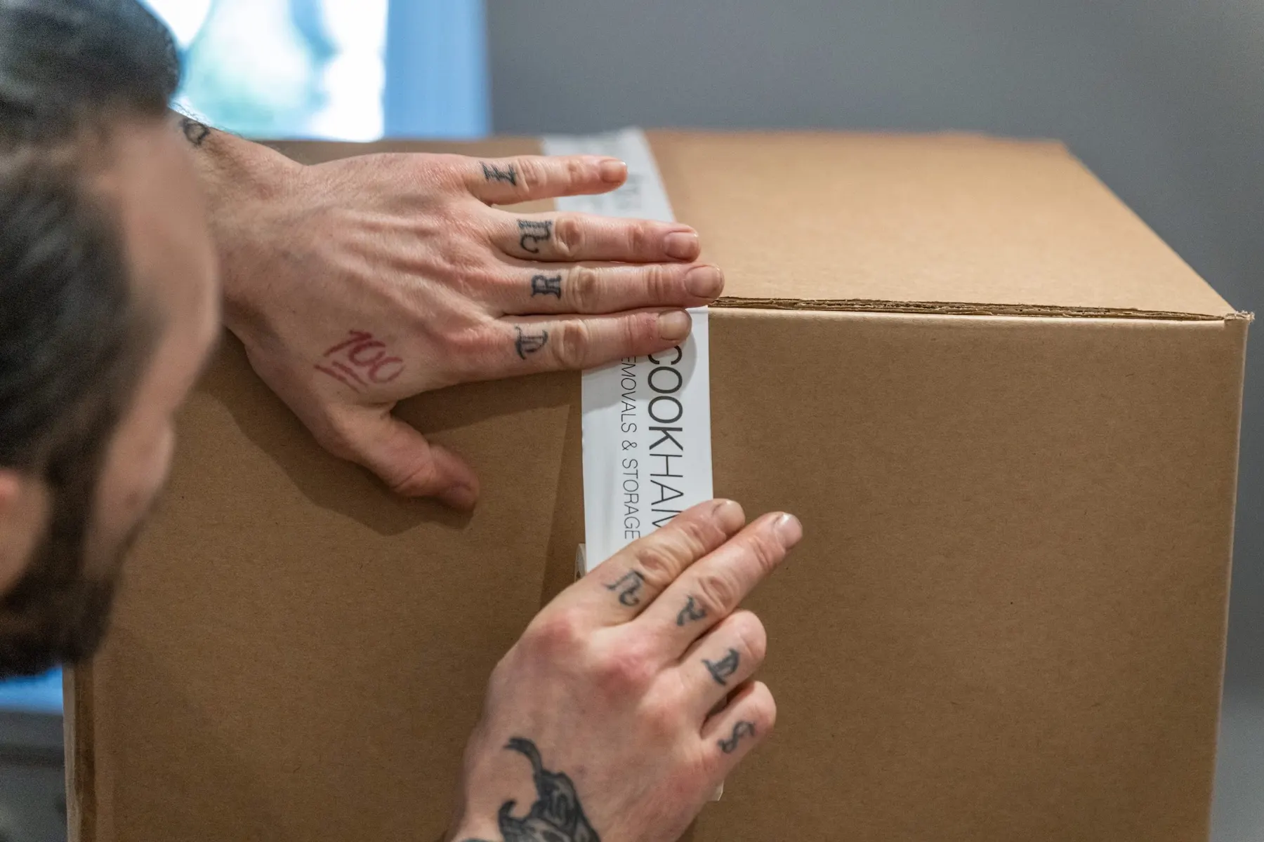Close-up of hands smoothing Cookham Removals & Storage branded tape across a cardboard box