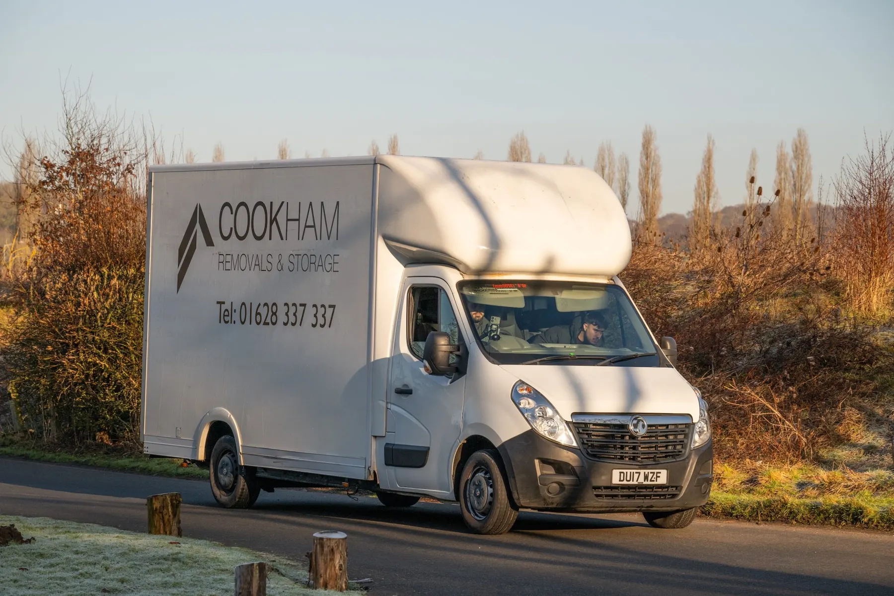 Cookham Removals & Storage Luton van driving along a tree-lined country lane in low winter sun