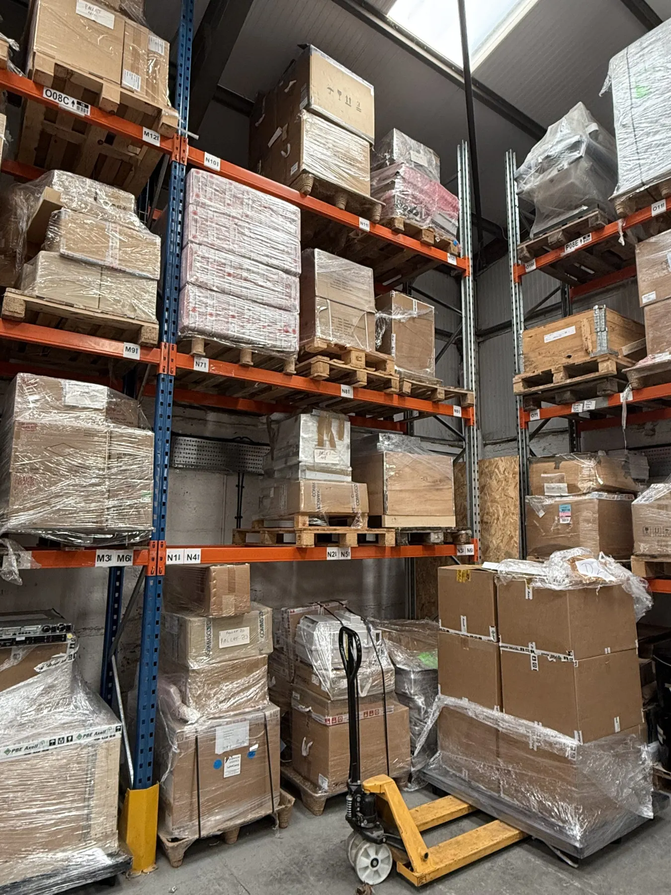 Warehouse pallet racking holding wrapped and boxed items, with a pallet truck in the aisle