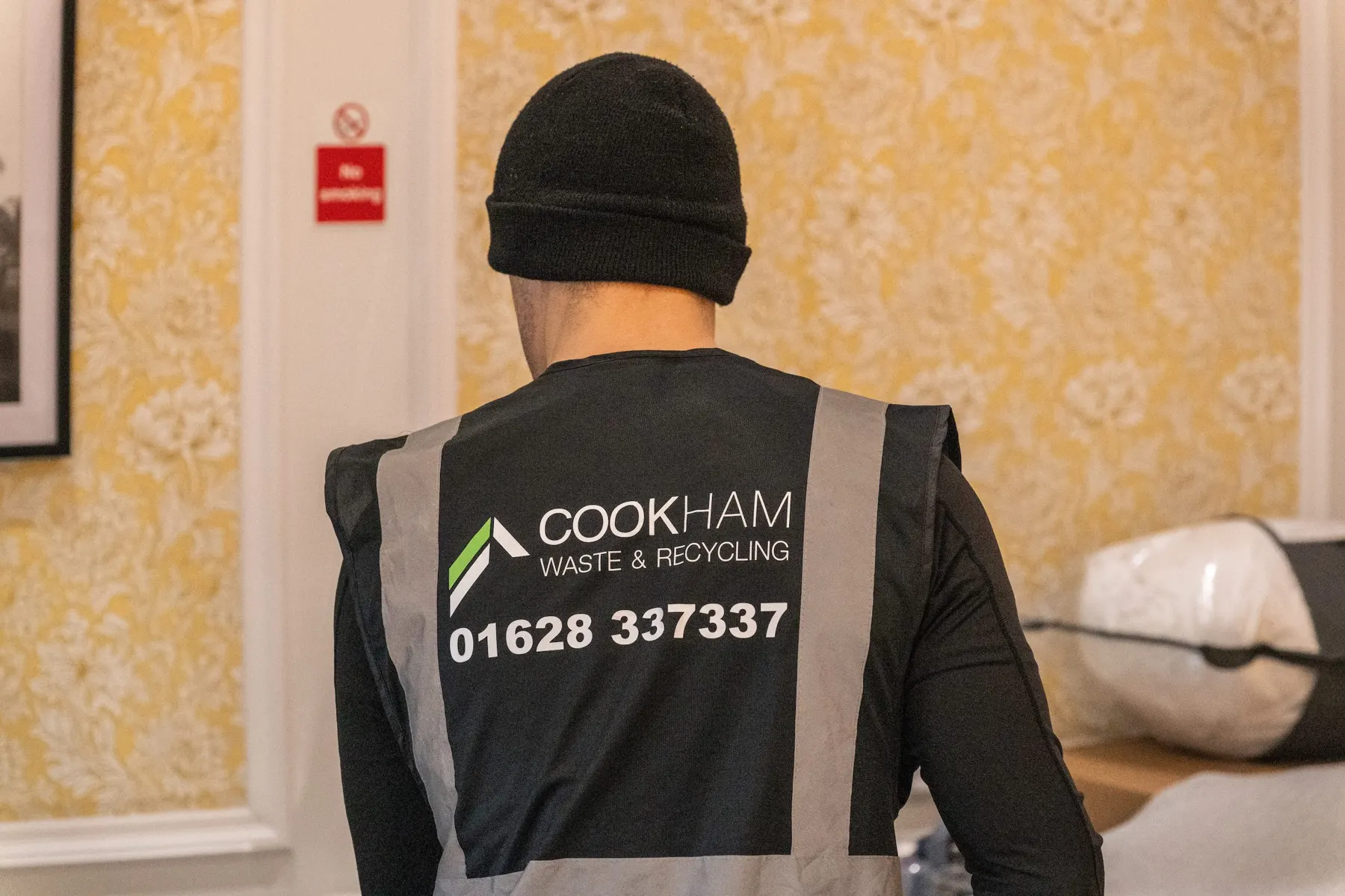 The back of a Cookham Removals & Storage crew member's grey vest showing the logo and phone number, inside a house