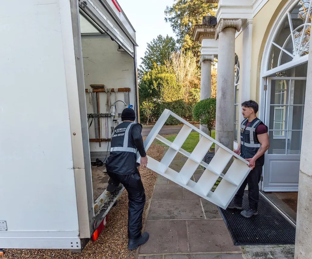 Two Cookham Removals & Storage crew members carrying a large frame between the Luton van and a pillared entrance