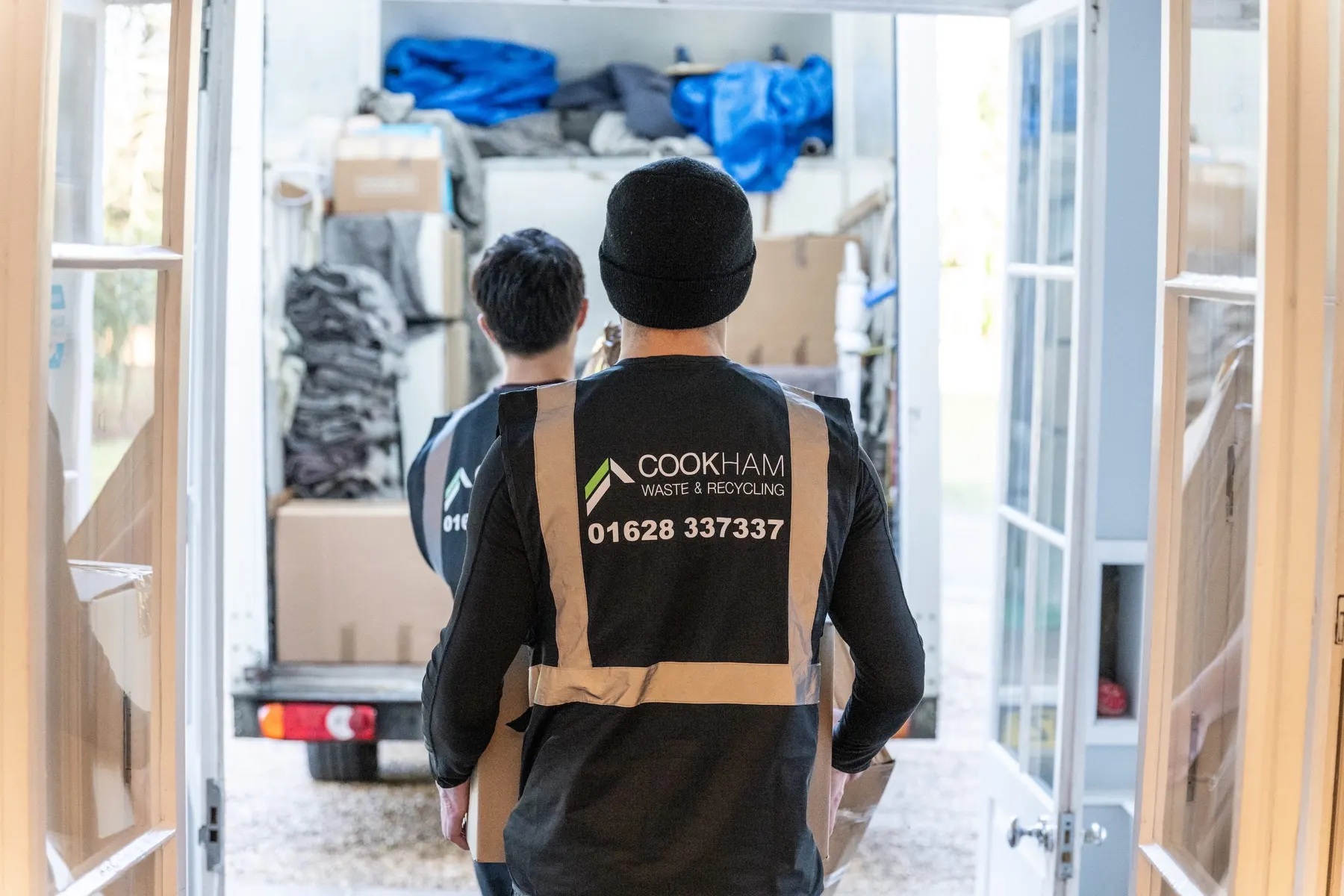 A Cookham Removals & Storage crew member in a branded grey vest walking towards the open Luton van