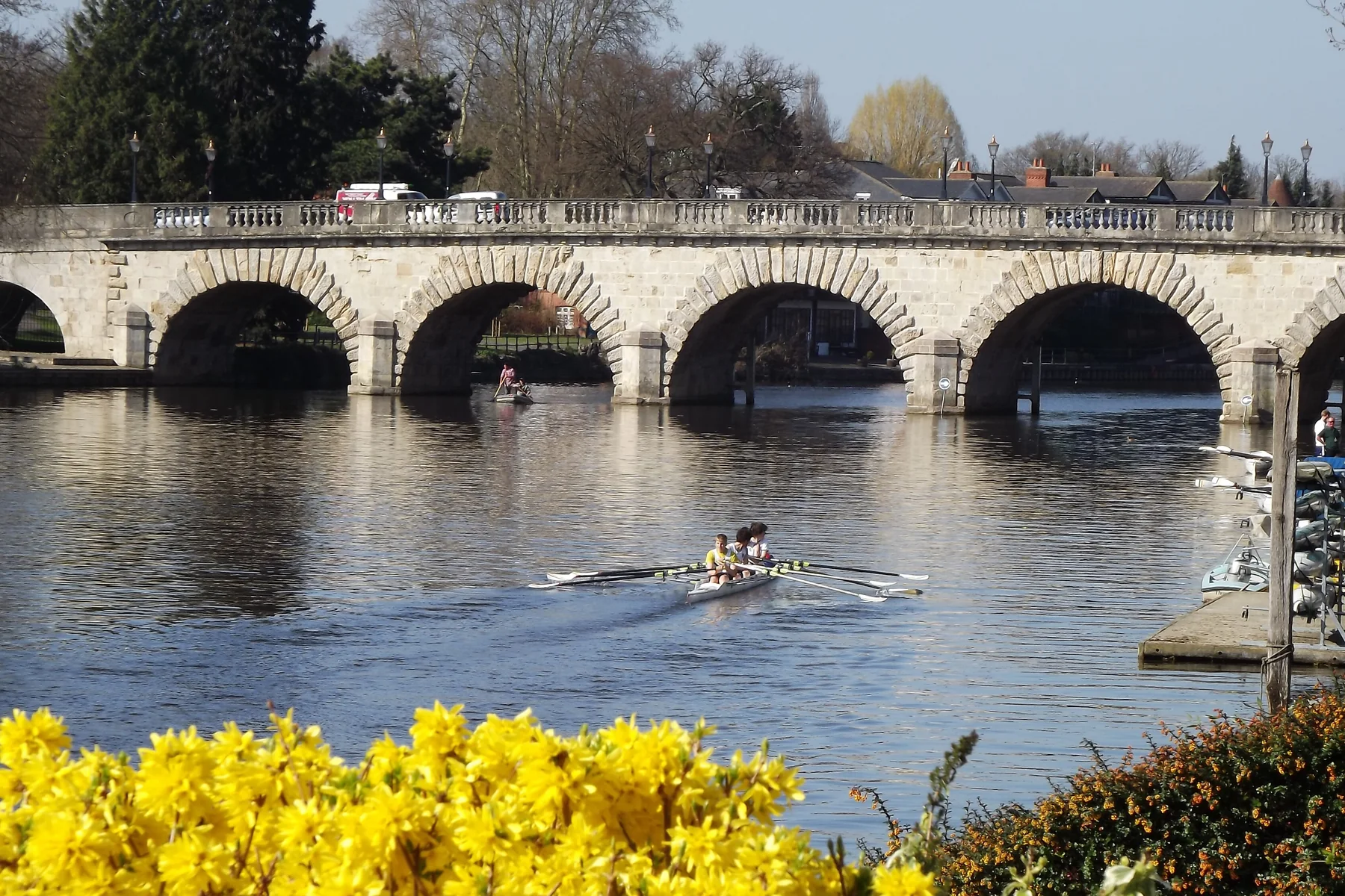 The stone arches of Maidenhead Bridge over the River Thames, with a rowing crew on the water